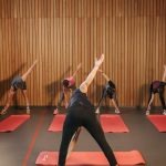 Yoga class with diverse adults stretching on mats in a cozy wooden studio.